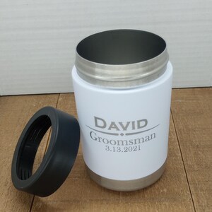 May include: White stainless steel can cooler with a black lid. The cooler has the name "DAVID" and the text "Groomsman 8.13.2021" engraved on it.