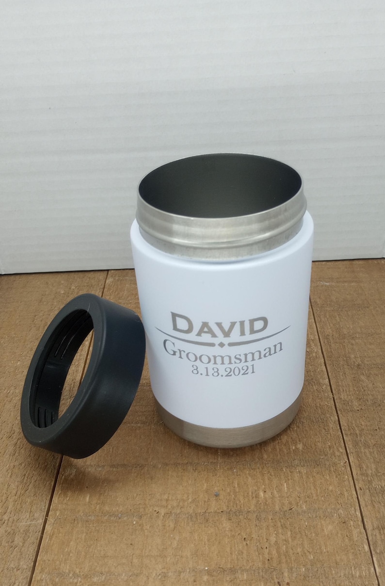 May include: White stainless steel can cooler with a black lid. The cooler has the name "DAVID" and the text "Groomsman 8.13.2021" engraved on it.