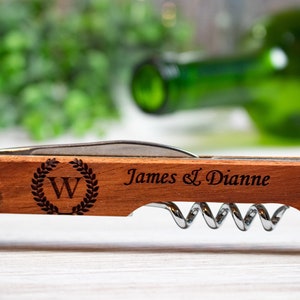 May include: A wooden wine opener with a silver corkscrew and bottle opener. The handle is engraved with the letter "W" in a wreath, and the text "James & Dianne".