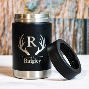 Op de afbeelding: Zwarte roestvrijstalen blikjeskoeler met een zwart rubberen deksel. De koeler heeft een zilveren gegraveerd ontwerp van geweien met de letter "R" in het midden en de naam "Ridgley" eronder.