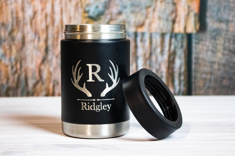 May include: Black stainless steel can cooler with a black rubber lid. The cooler has a silver engraved design of antlers with the letter "R" in the center and the name "Ridgley" below.