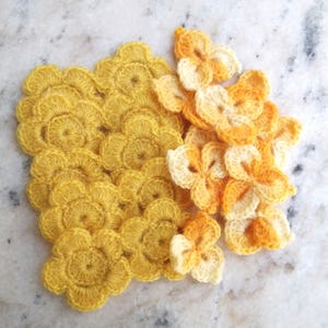 Pode incluir: Uma coleção de pequenas aplicações de flores em crochê em vários tons de amarelo e laranja. O grupo inclui flores amarelas planas e circulares com bordas recortadas e flores tridimensionais em camadas com pétalas.