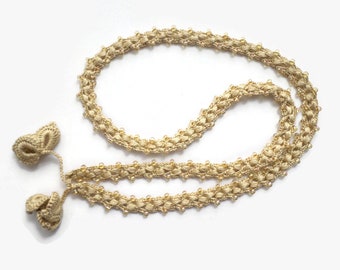 May include: A beige crocheted necklace with small beads and two tassels. The necklace is made of a delicate, intricate pattern.