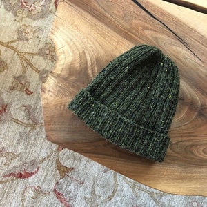 Könnte beinhalten: Eine dunkelgrüne Strickmütze mit einer melierten Textur.