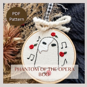 May include: Embroidered hoop art featuring a white ghost with a black mask, red roses, and musical notes. The text "PHANTOM OF THE OPERA BOO" is below the hoop.