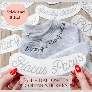 May include: A light grey crewneck sweatshirt featuring the embroidered text Midnight Margaritas in black thread. The sweatshirt is surrounded by several white adhesive collar stickers with various Halloween phrases like Hocus Pocus.