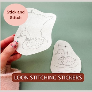 May include: Two white, die-cut stickers with loon designs. One sticker features a loon outline within a state outline, the other shows a loon with stars. The text "Stick and Stitch" and "LOON STITCHING STICKERS" are also visible.