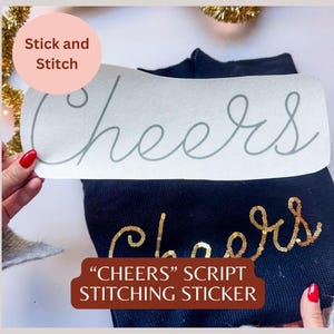 May include: A navy blue sweater with a gold sequin "Cheers" script design. A white sticker with a gray "Cheers" script is held above the sweater. The image also includes text that says "Stick and Stitch" and ""Cheers" Script Stitching Sticker".