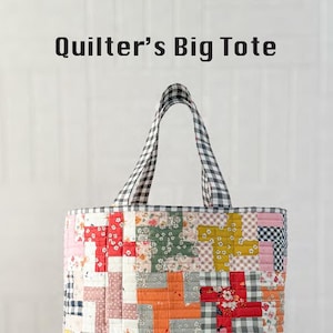 May include: A large, reversible tote bag with a patchwork design. The bag features a variety of floral and geometric patterns in red, pink, yellow, and green. The handles are a black and white gingham check. The text "Quilter's Big Tote" is at the top.
