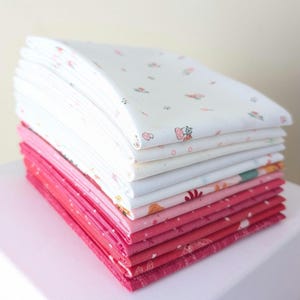 May include: A stack of folded fabric squares in shades of pink and white. The top layers are white with a delicate floral pattern in pink and green. The lower layers transition from light to deep pink.