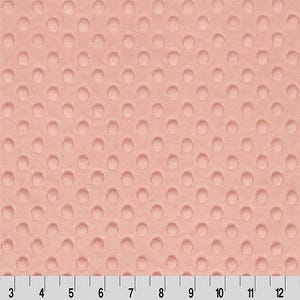 May include: Close-up of a peach-colored fabric with a raised dot pattern. The fabric has a soft, textured appearance. A ruler is at the bottom, showing measurements in inches.
