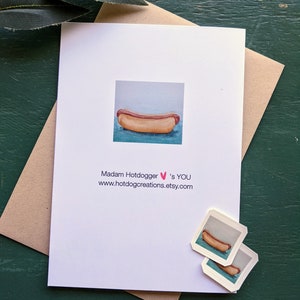 May include: A white card with a watercolor illustration of a hot dog on a blue background. The text on the card reads "Madam Hotdogger &hearts;'s YOU www.hotdogcreations.etsy.com".