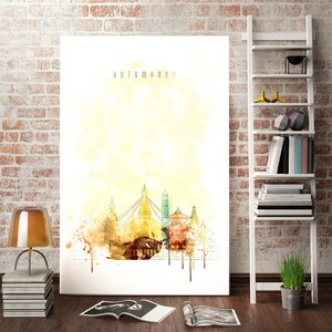 Puede incluir: Una gran impresión en lienzo con una ilustración en acuarela de Katmandú, Nepal. La obra de arte muestra monumentos emblemáticos con una cálida paleta de colores amarillos, marrones y verdes. La palabra "KATHMANDU" está impresa en la parte superior.