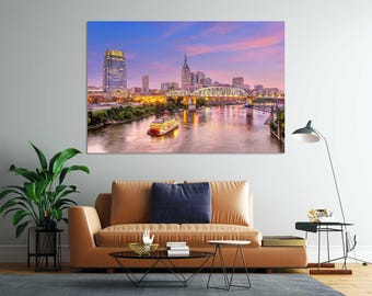 May include: A large rectangular wall art print featuring a twilight cityscape of Nashville, Tennessee, with the Cumberland River, the John Seigenthaler Pedestrian Bridge, a paddlewheel riverboat, and illuminated skyscrapers under a pink and blue sky.