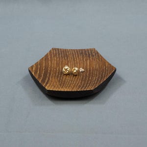 May include: A pair of gold knot-shaped earrings on a dark brown wooden tray.
