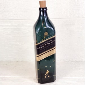 May include: A green glass bottle with a gold label that reads "Johnnie Walker Double Black Blended Scotch Whisky". The bottle is decorated with gold glitter and has a cork stopper.