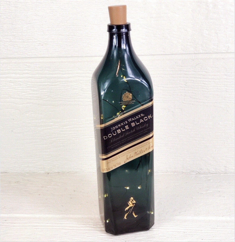 May include: A green glass bottle with a gold label that reads "Johnnie Walker Double Black Blended Scotch Whisky". The bottle is decorated with gold glitter and has a cork stopper.