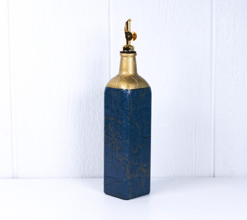 May include: A blue glass bottle with a gold top and a gold design. The bottle has a spout for dispensing liquids.