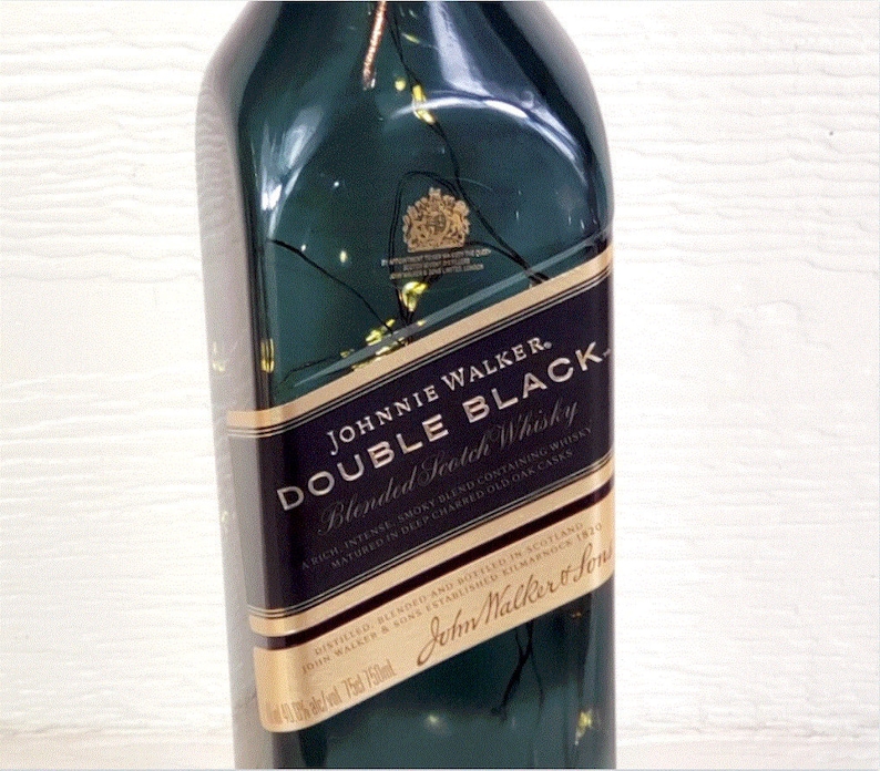 May include: A green glass bottle of Johnnie Walker Double Black Blended Scotch Whisky. The label is gold and black with the text "JOHNNIE WALKER. DOUBLE BLACK Blended Scotch Whisky A rich, intense, smoky blend containing whisky matured in deep charred old oak casks" and "DISTILLED, BLENDED AND BOTTLED IN SCOTLAND JOHN WALKER & SONS ESTABLISHED KILMARNOCK 1820 John Walker & Sons".