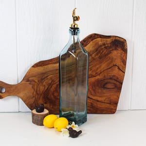 May include: A clear glass bottle with a gold spout and a black stopper. The bottle is sitting on a wooden cutting board. There are lemons and small bird figurines in the foreground.
