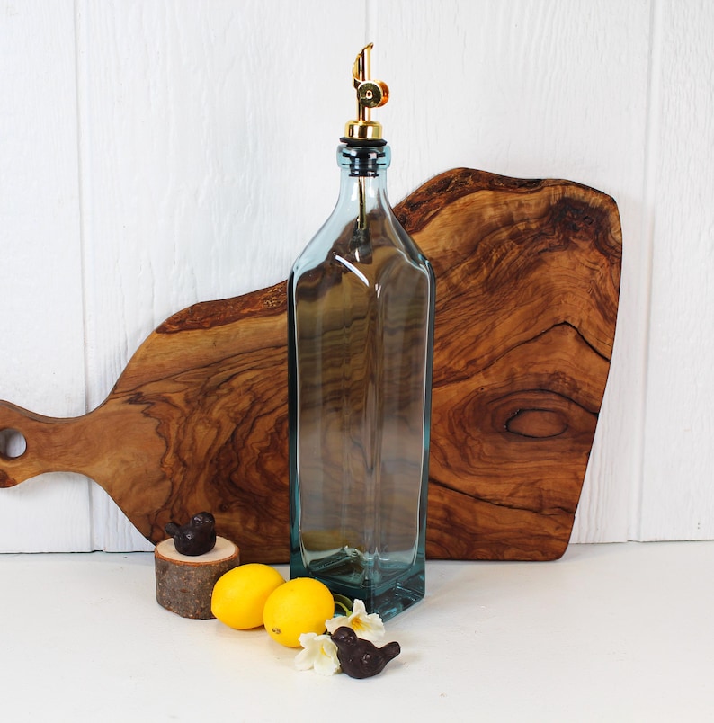 May include: A clear glass bottle with a gold spout and a black stopper. The bottle is sitting on a wooden cutting board. There are lemons and small bird figurines in the foreground.