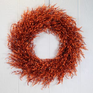 Pode incluir: Uma grande coroa redonda de cor laranja feita de vegetação artificial. A coroa é feita de pequenas folhas delicadas e é perfeita para adicionar um toque de cor outonal à decoração da sua casa.