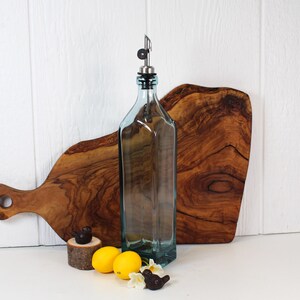 May include: A clear glass bottle with a silver spout and a blue tint. The bottle is sitting on a wooden cutting board. There are two small bird figurines and lemons in the foreground.