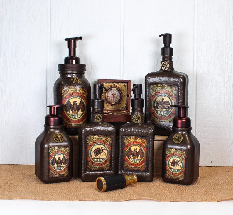 K&ouml;nnte beinhalten: Eine Sammlung von sechs dunkelbraunen Seifenspendern im Apothekerstil mit Pumpverschluss, die mit Vintage-Etiketten von Flederm&auml;usen, Spinnen und Schlangen versehen sind. Dahinter befinden sich eine kleine Holzkiste mit Uhr und ein Messingfernrohr.