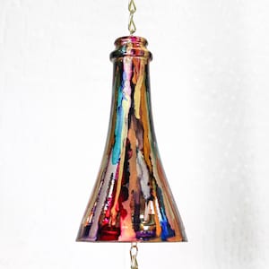 May include: A handcrafted wind chime made from a repurposed glass bottle. The bottle is painted with vibrant colors including red, blue, yellow, and brown. The bottle is suspended by a gold-colored chain.