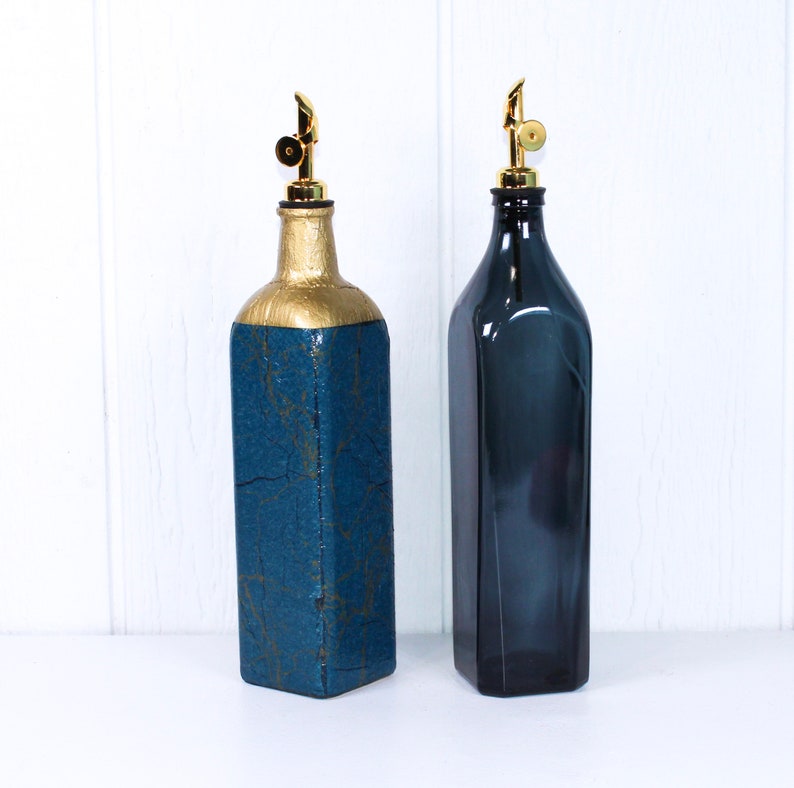 May include: Two blue glass bottles with gold tops and spouts. The bottle on the left has a textured blue finish. The bottle on the right is a solid blue colour.