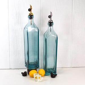May include: Two blue glass bottles with pour spouts and stoppers. The bottles are on a white surface with lemons and small decorative birds.