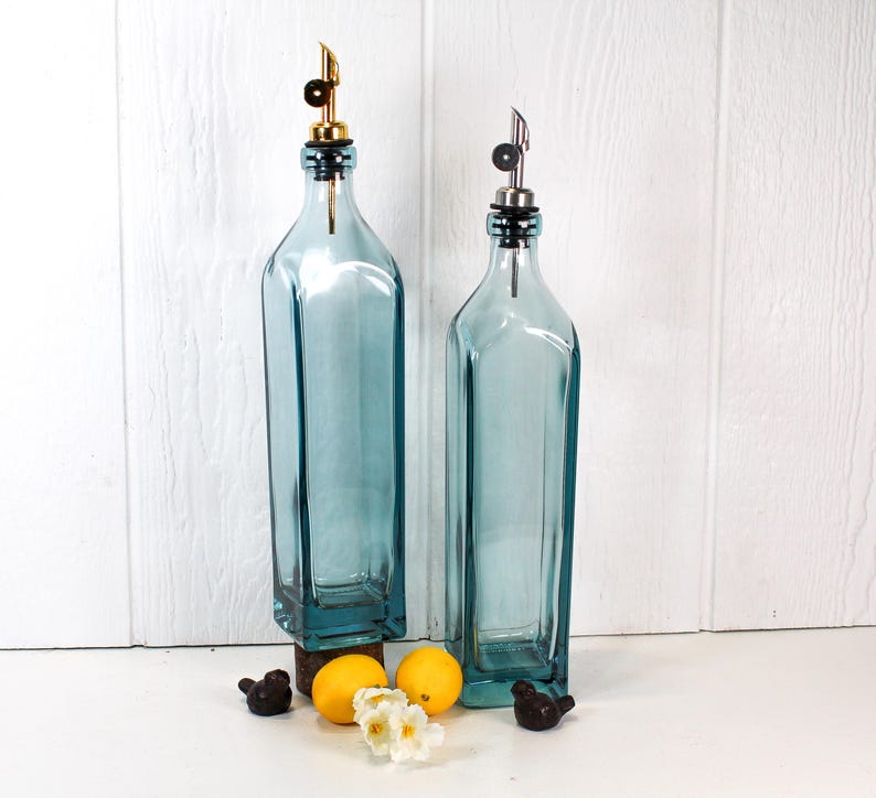 May include: Two blue glass bottles with pour spouts and stoppers. The bottles are on a white surface with lemons and small decorative birds.