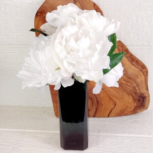 May include: A bouquet of white peonies arranged in a dark green vase. The vase is sitting on a wooden cutting board.