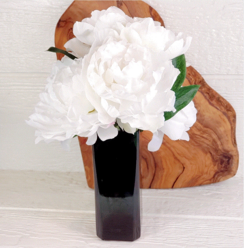 May include: A bouquet of white peonies arranged in a dark green vase. The vase is sitting on a wooden cutting board.