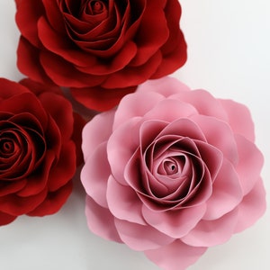 Puede incluir: Tres rosas de papel, una roja, una rosa y una rojo oscuro, est&aacute;n dispuestas sobre un fondo blanco. Las rosas est&aacute;n hechas de papel y tienen un aspecto tridimensional.