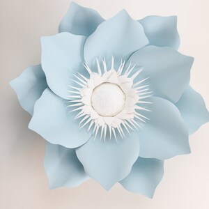 Pu&ograve; includere: Un grande fiore di carta blu chiaro con un centro bianco. Il fiore ha molti petali ed &egrave; fatto di carta.