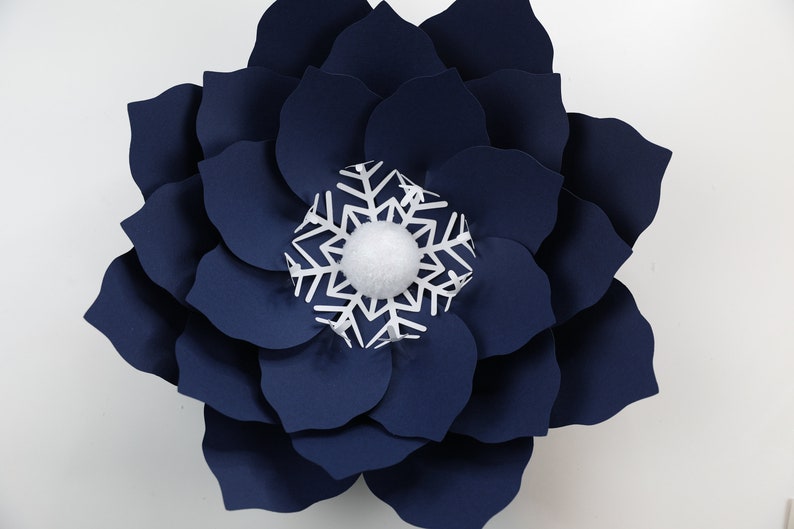Pu&ograve; includere: Un grande fiore di carta blu navy con un fiocco di neve bianco e un pon pon bianco al centro.