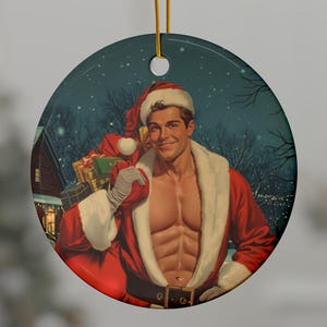 May include: Round Christmas ornament featuring a vintage illustration of a muscular Santa Claus figure in a red suit and hat, carrying a sack of gifts. The background shows a snowy scene with a house and trees.