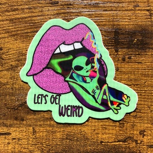May include: A sticker featuring a cartoon alien smoking a cigarette inside a mouth with purple lips. The sticker has a green border and the text "LET'S GET WEIRD" in green.