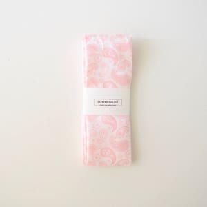 May include: A pink paisley patterned fabric tie with a white label that reads "SUMMERBREEZE" in black text.