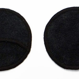 Pode incluir: Duas almofadas redondas pretas para remover maquiagem. Uma almofada tem um corte no centro.