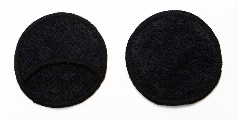 Pode incluir: Duas almofadas redondas pretas para remover maquiagem. Uma almofada tem um corte no centro.