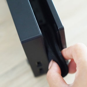 Pode incluir: Um dispositivo eletr&ocirc;nico preto com uma capa de tecido preto sendo puxada para fora do dispositivo. O dispositivo possui v&aacute;rias portas no lado.