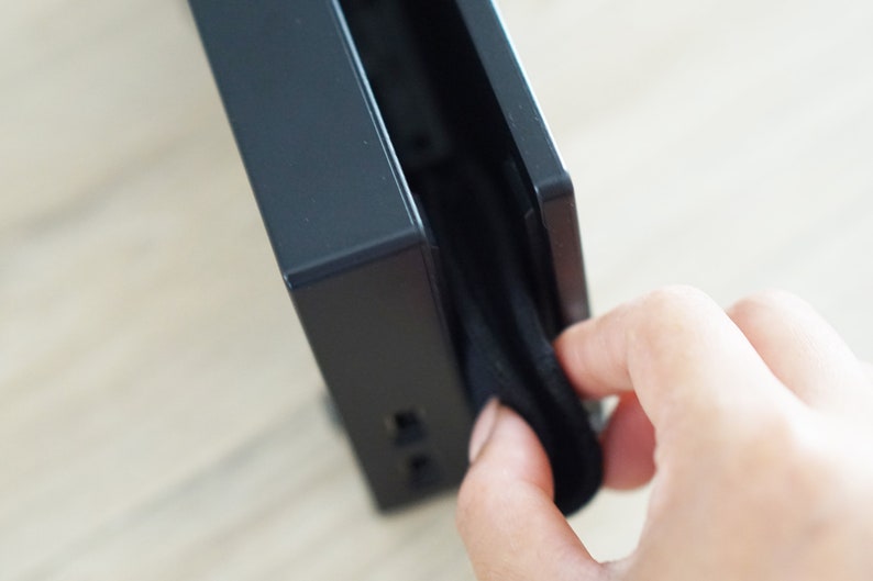 Pode incluir: Um dispositivo eletr&ocirc;nico preto com uma capa de tecido preto sendo puxada para fora do dispositivo. O dispositivo possui v&aacute;rias portas no lado.