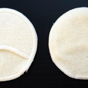 Pode incluir: Duas almofadas de mama reutiliz&aacute;veis redondas brancas. Uma almofada tem uma pequena abertura no centro.