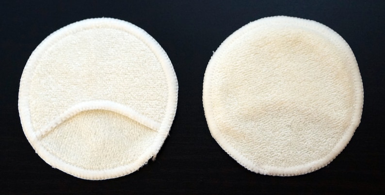 Pode incluir: Duas almofadas de mama reutiliz&aacute;veis redondas brancas. Uma almofada tem uma pequena abertura no centro.