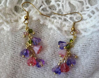 May include: A pair of dangle earrings with gold-colored hooks. Each earring features a cluster of small, translucent flower-shaped beads in shades of purple, pink, and red, accented with green and clear beads. The earrings are set against a white, textured background.