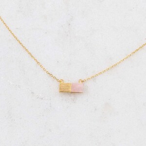May include: A delicate gold chain necklace with a small pink and gold rectangular pendant.
