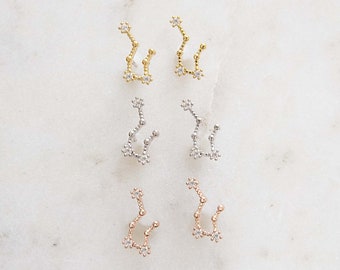 May include: Three pairs of constellation earrings in gold, silver, and rose gold. Each pair features a constellation design with small clear stones.