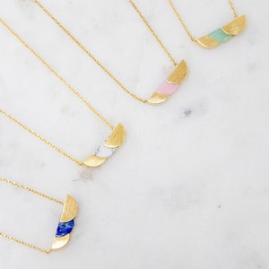 May include: Four gold necklaces with different colored stone pendants. Each pendant is made of three crescent-shaped pieces, with the top piece being gold and the bottom two pieces being the colored stone. The stones are green, pink, white, and blue.